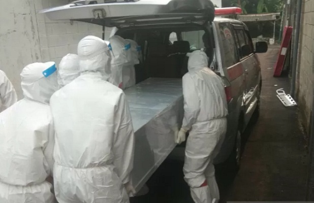 Petugas memasukan peti jenazah ke dalam ambulans untuk dimakamkan